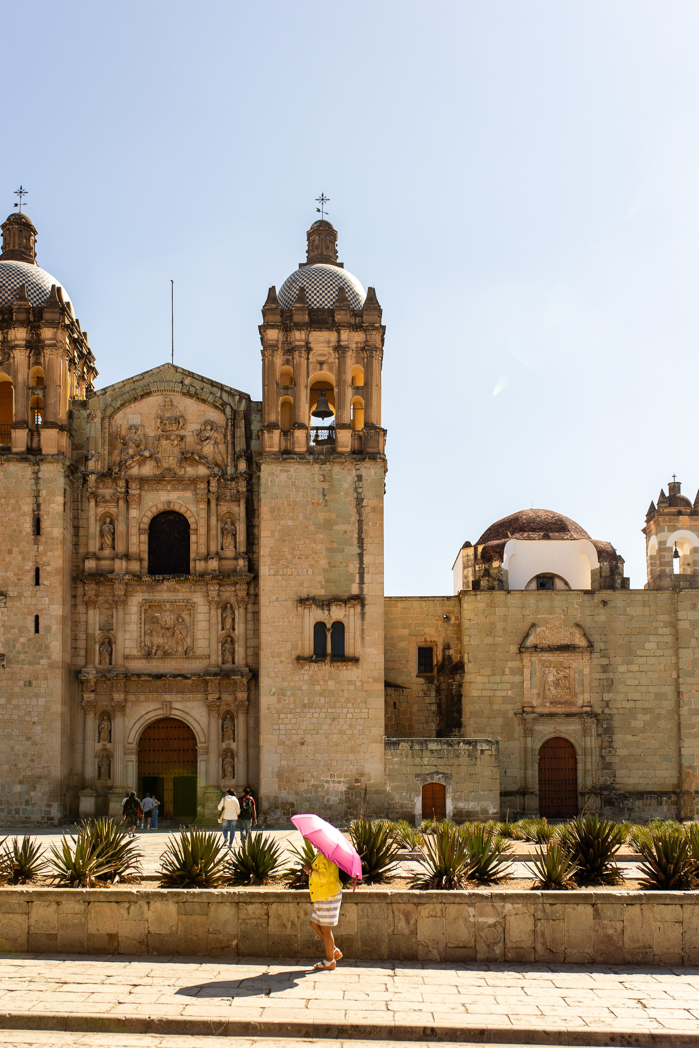 woman with an umbrella walking in front of church in Oaxaca
