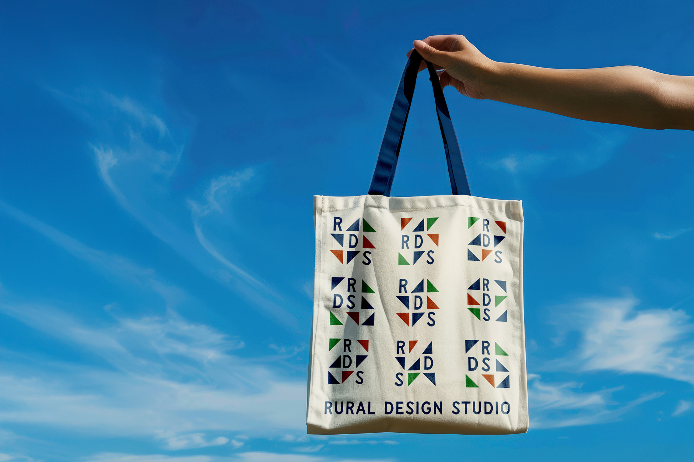 Rural Design Studio tote bag being held by an arm against a blue sky